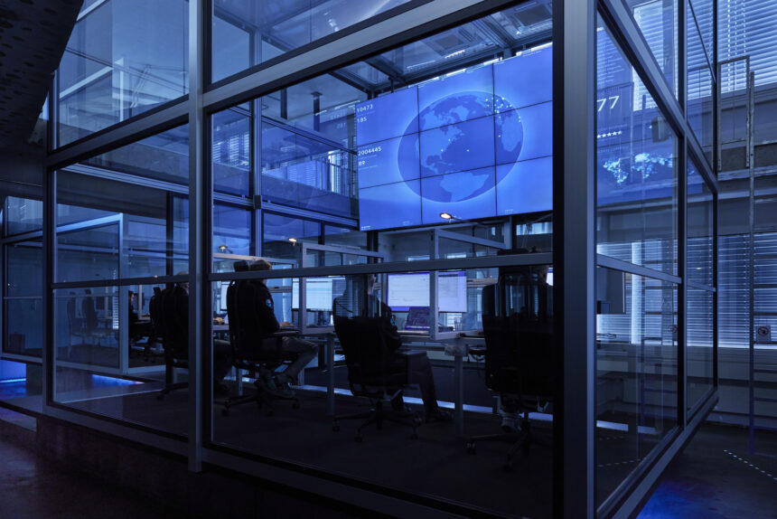 Open Systems Mission Control: engineers at desks behind glass, a world map on the wall of screens