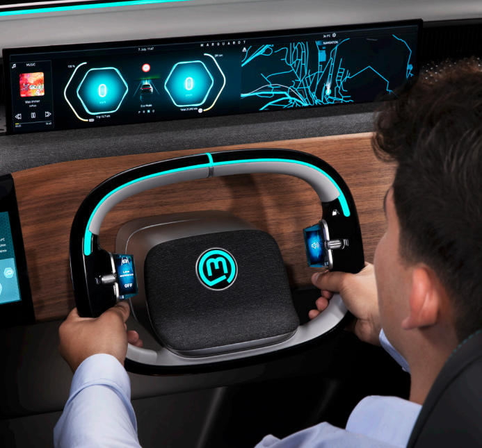 A driver's hands on a Marquardt concept steering wheel with illuminated controls and cockpit displays